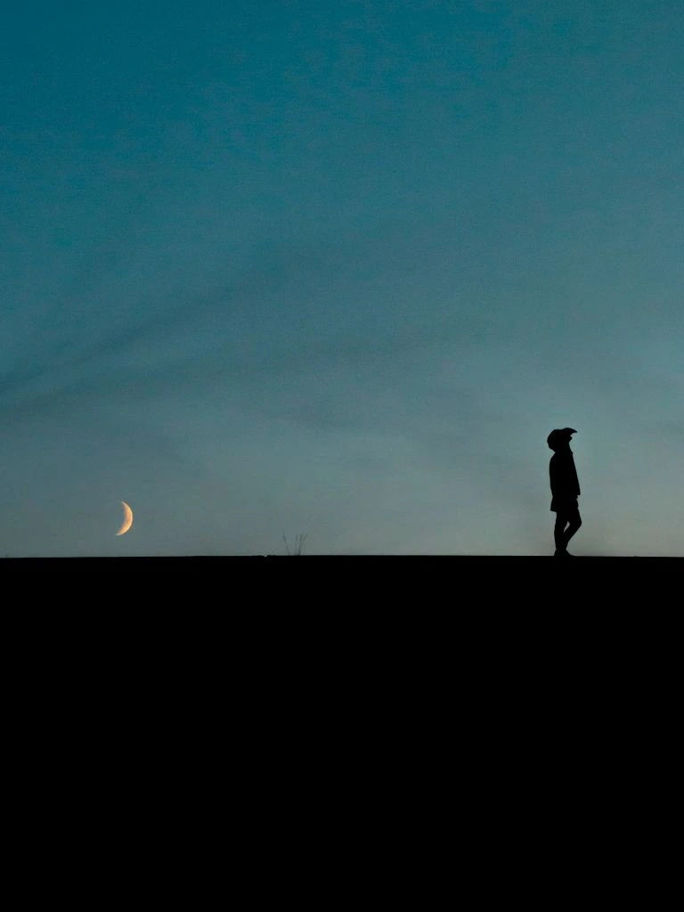 A solitary figure stands at the end of a weathered pier under heavy fog
