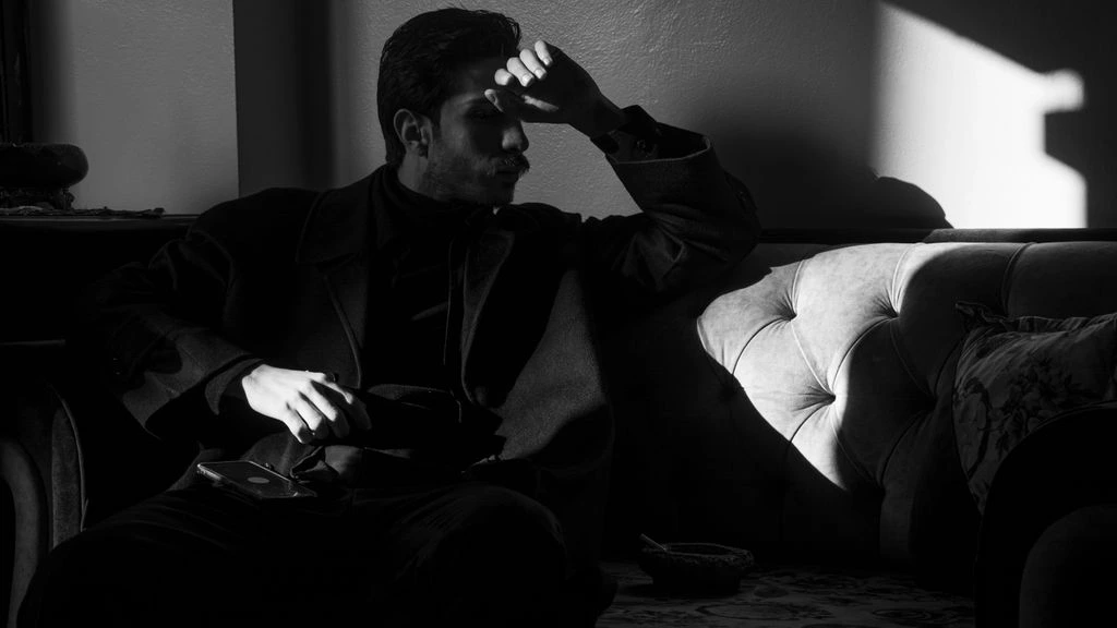 A young man sits alone in a sunlit apartment